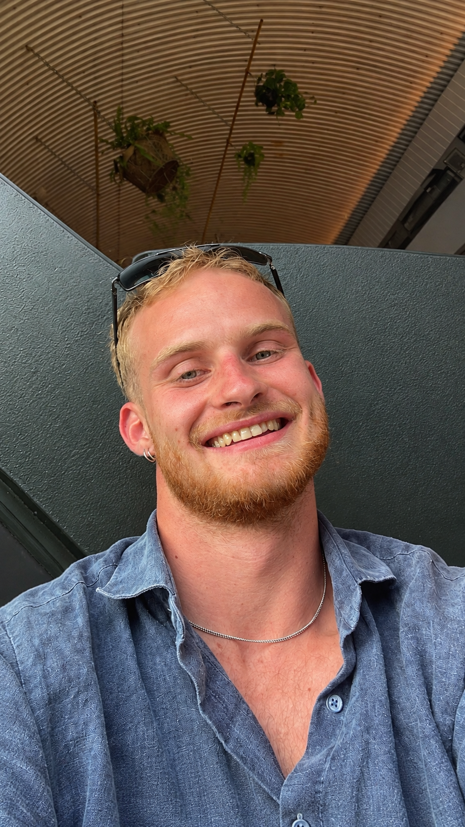 Portrait of Fred Stephens smiling, sunglasses resting on his head, in a corrugated-roof shelter